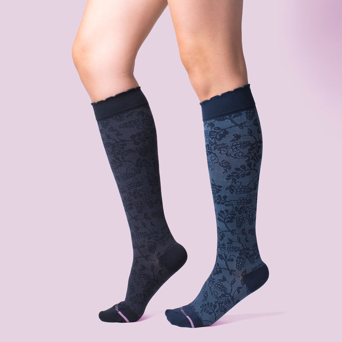 Knee-high compression socks with a grape vine pattern in dark blue and a scalloped top.