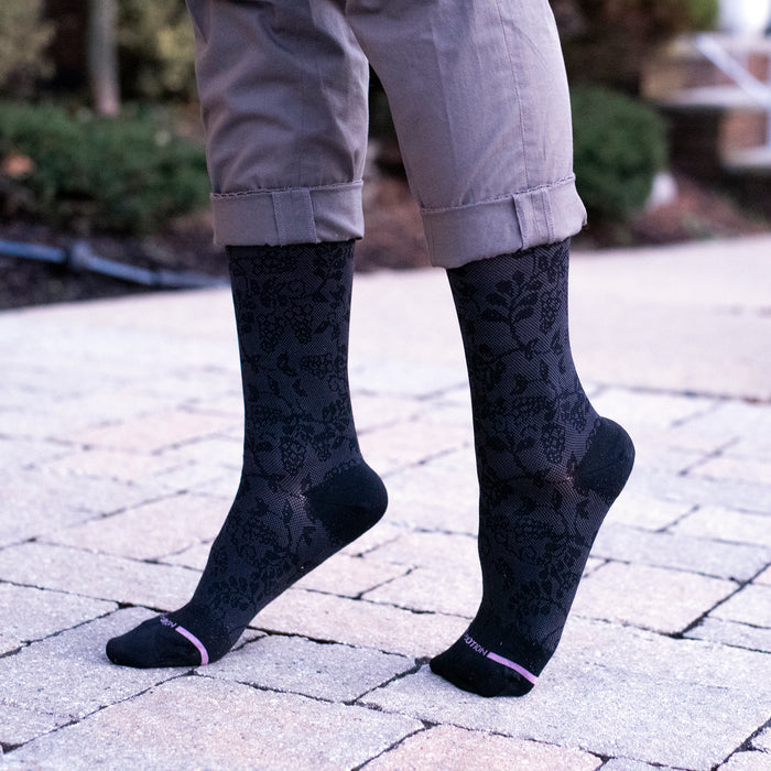 Knee-high compression socks with a grape vine texture, worn with rolled-up pants on a stone surface.