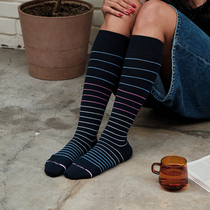 Knee-high compression socks with multi-color pinstripes worn by a person sitting on a concrete floor.