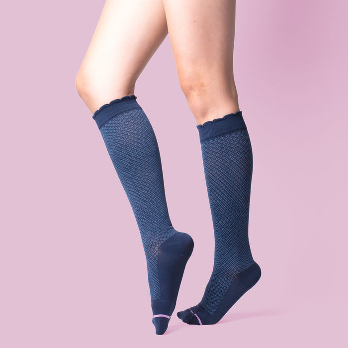 Knee-high compression socks in navy with a textured pattern and scalloped top, displayed against a pink background.
