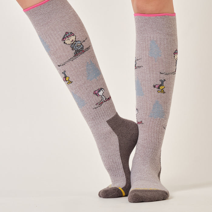 Wine marl knee-high compression socks with a Peanuts ski trip design, worn in a snowy outdoor setting.