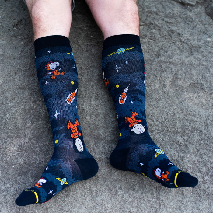 Navy knee-high compression socks for men with Snoopy and Charlie Brown space designs, worn in a lifestyle setting.